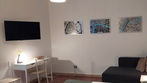Une pièce comprenant un bureau, un canapé noir et trois cartes de Paris, de Londres et de New York accrochées au mur.