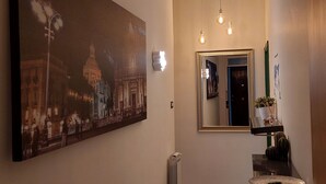 Un couloir orné d’un grand tableau représentant un paysage urbain, d’un miroir et d’une petite table sur laquelle est posée une plante.