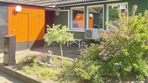 Une maison avec un toit en tuiles, un petit jardin orné d’une statue de grenouille et une fenêtre sur laquelle on peut lire l’inscription « MI ».