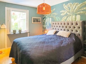 A bedroom with a large bed, a window with blinds, a hanging orange light fixture, and a wall with a leafy pattern. - 4 Star Holiday Home in Vastervik (Vastervik)