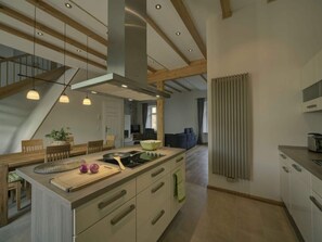 A modern kitchen with a central island, wooden beams, and pendant lighting. - Holiday Apartment Goose in the Monument (Maring-Noviand)