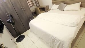 Ein Schlafzimmer mit Bett, Kleiderschrank, Nachttisch und Ventilator.