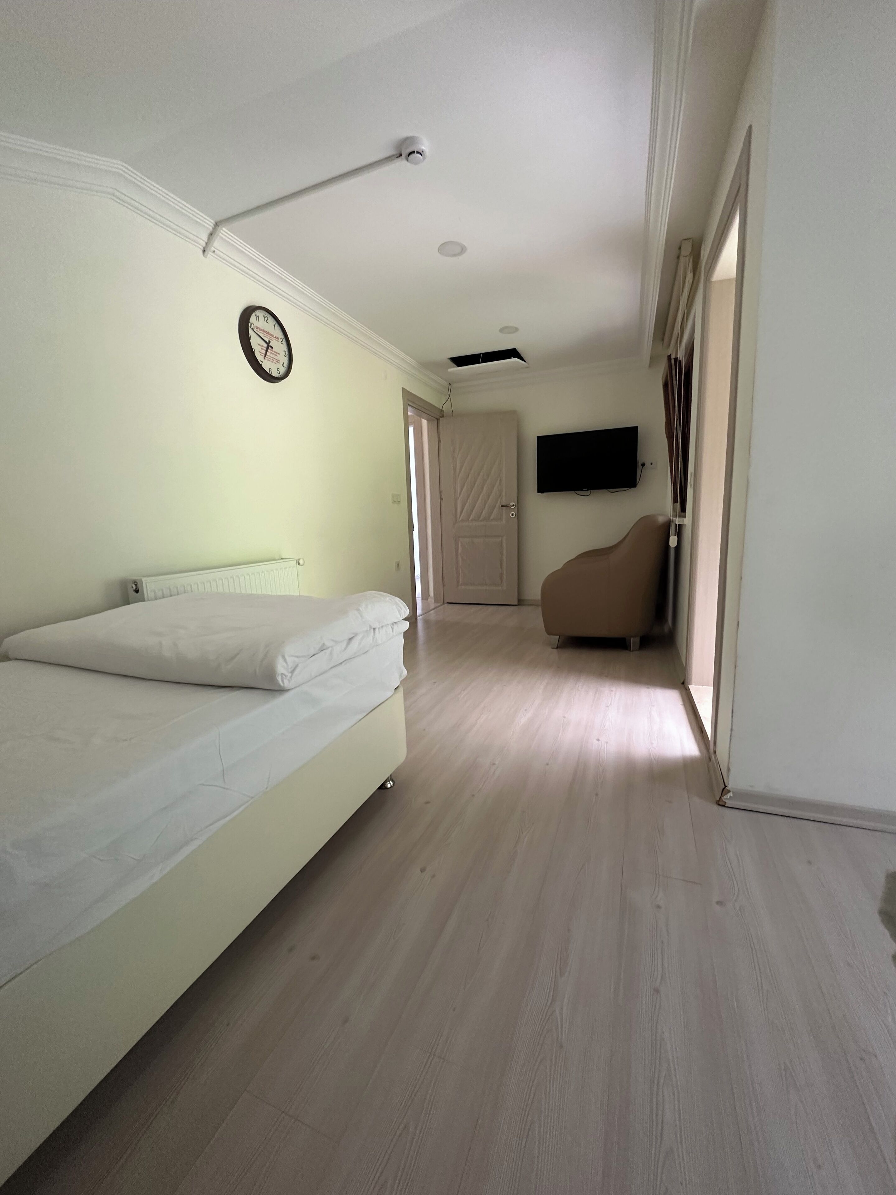A bedroom with a bed, a wall clock, a television, and a door leading to another room.