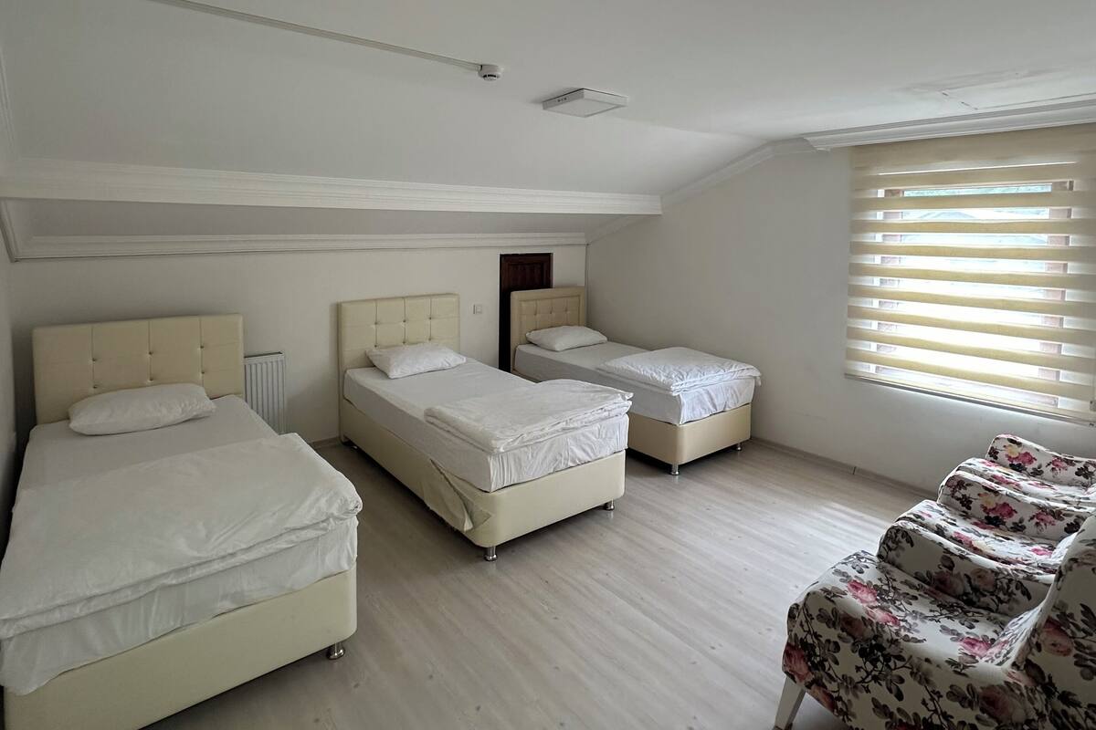 A bedroom with three beds, a radiator, a window with blinds, and a floral chair.