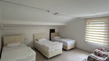 Un dormitorio con tres camas, un radiador, una ventana con persianas y una butaca con estampado floral.