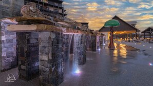 A stone waterfall structure with a wooden building in the background and a covered seating area. - Luxury Chalet | Indoor pool | Hot Tub | Game Room (Sevierville)