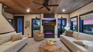 A modern living room with two sofas, a coffee table, a fireplace, and a large TV. - Luxury Chalet | Indoor pool | Hot Tub | Game Room (Sevierville)