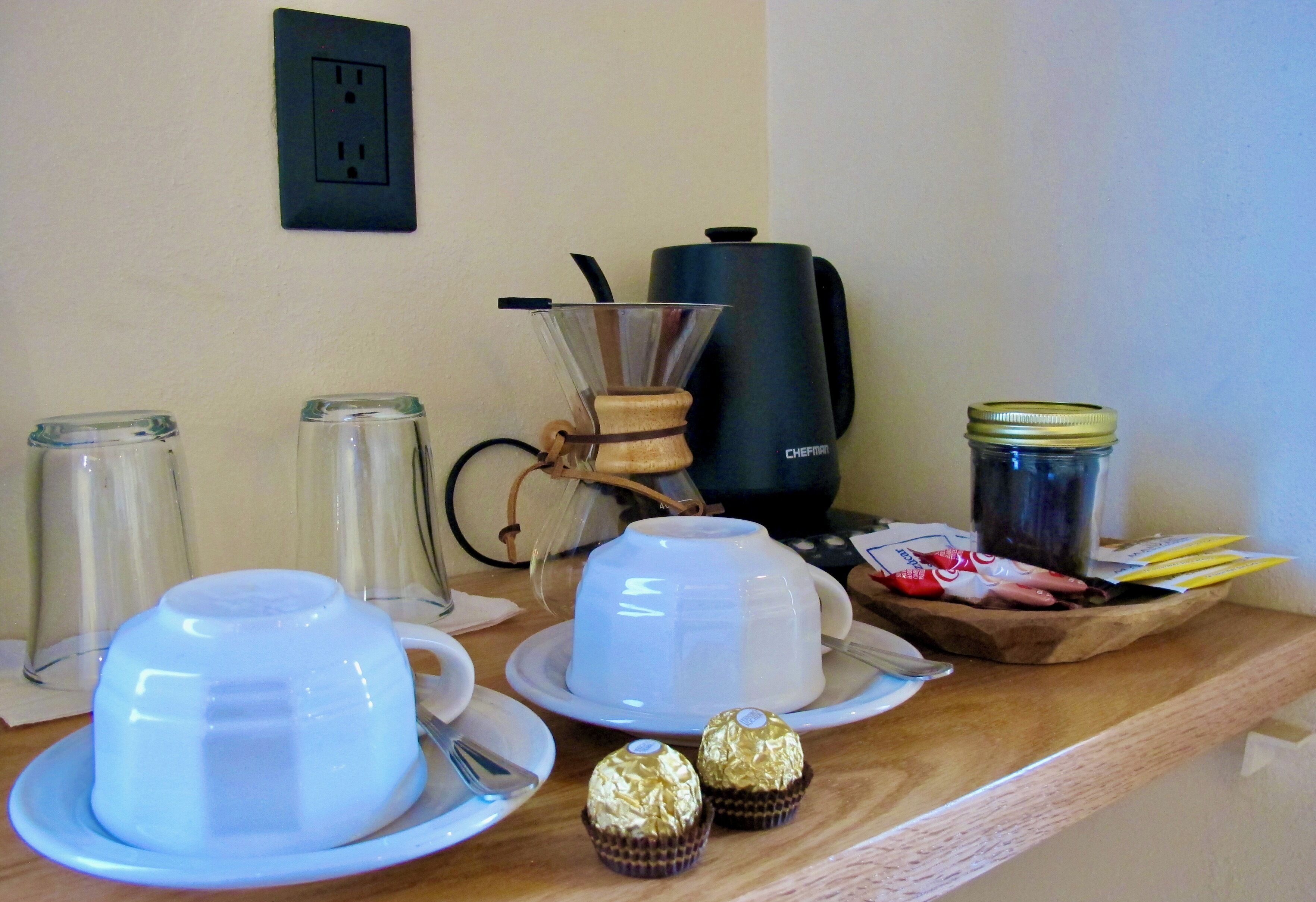 Een aanrecht met koffiezetapparatuur, waaronder een koffieapparaat, een cafetière en een koffiekan. Ook staan er twee glazen potten en een pot met deksel op het aanrecht.