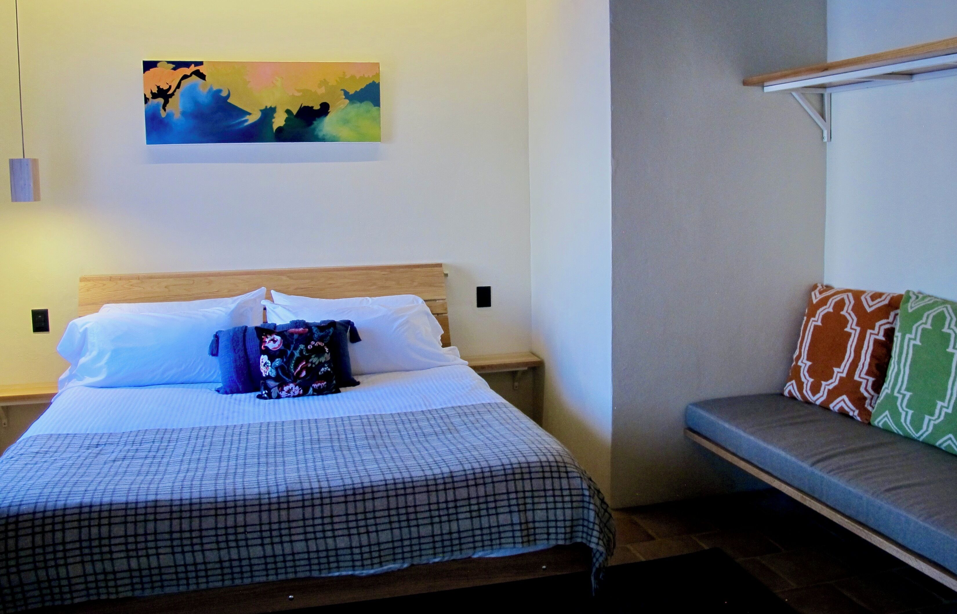 A bedroom with a bed, a bench, a painting, and a nightstand.