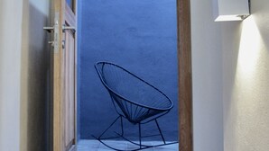 A narrow hallway with a wooden door leading to a room with a blue wall and a chair.