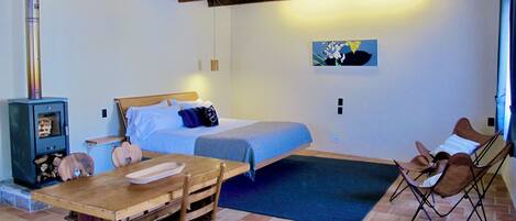 Una habitación acogedora con una cama, una mesa y dos sillas. Hay un armario de madera con un estante y una lámpara colgante.