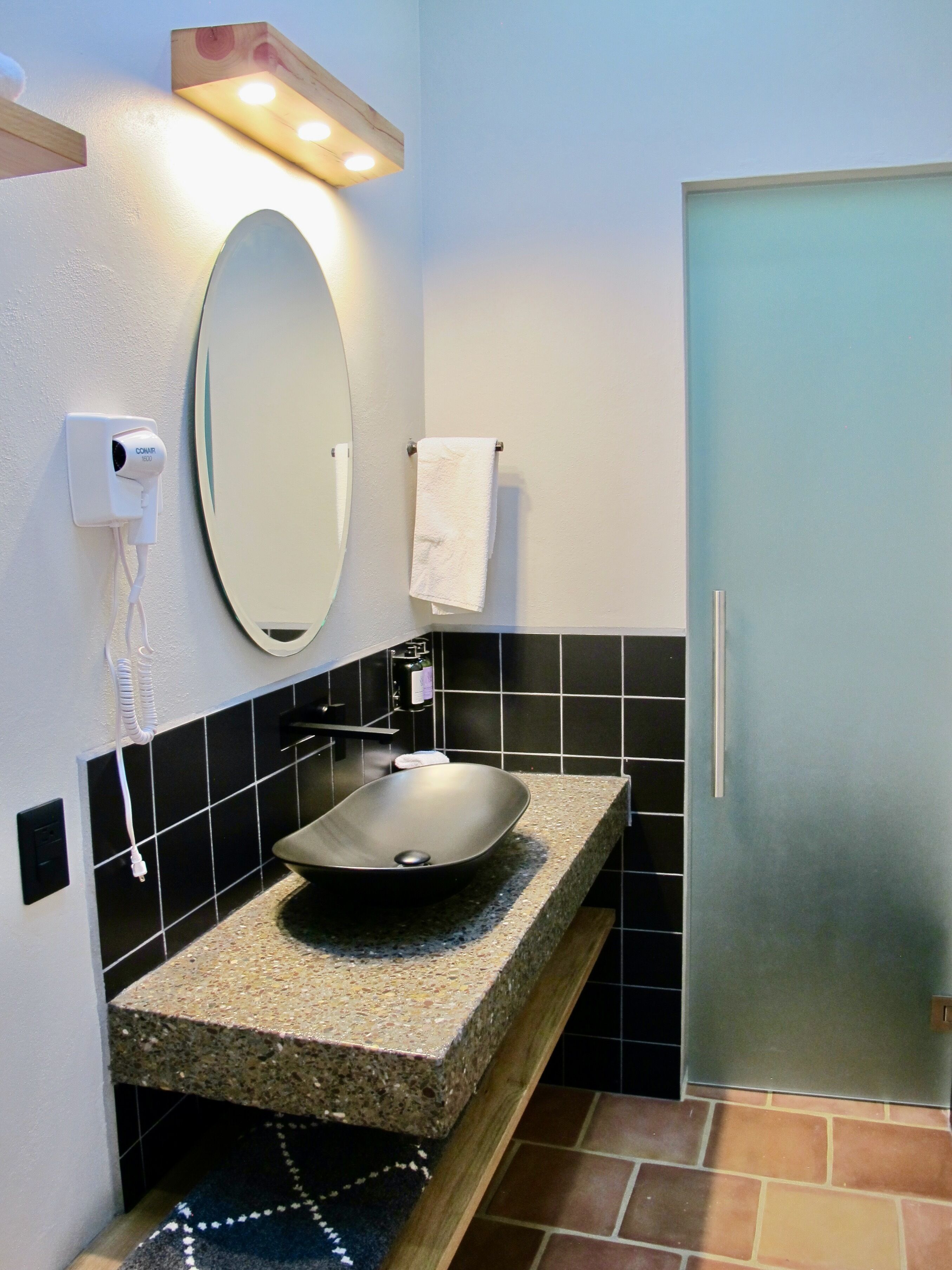 A bathroom with a granite countertop, a vessel sink, a mirror, a towel rack, and a door.