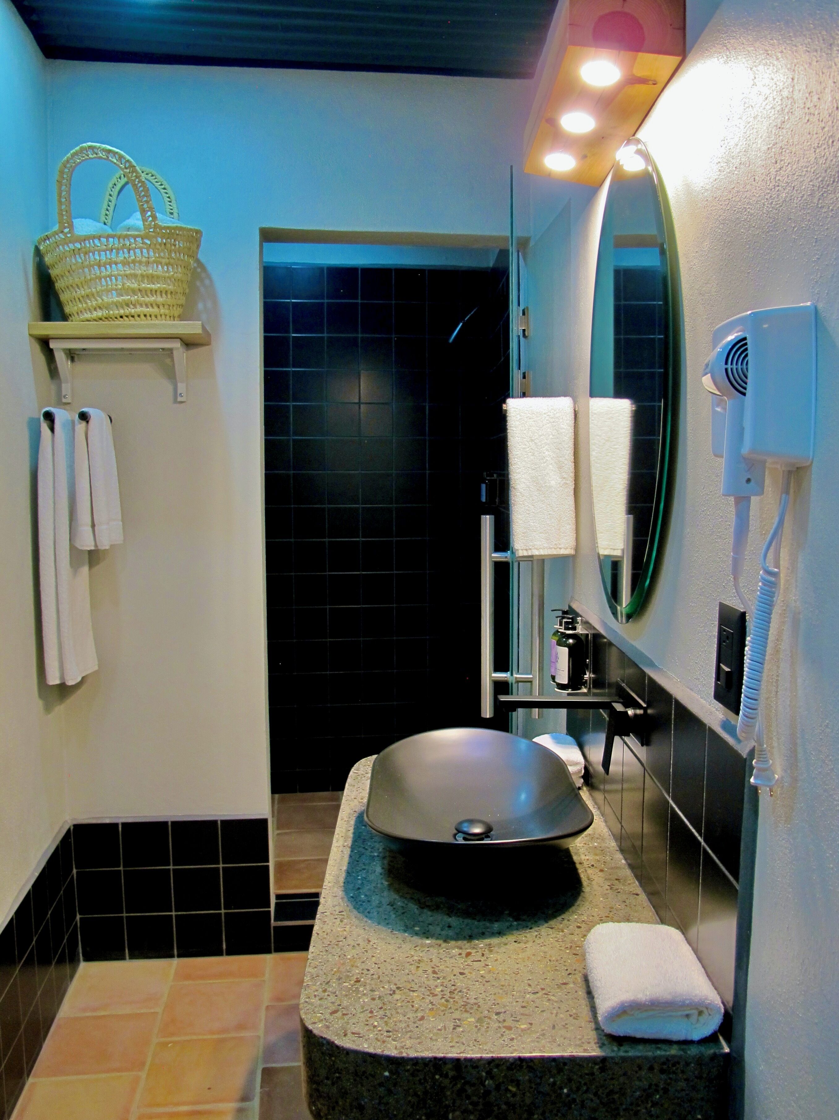 Un baño con un espejo grande, un lavabo, una toalla, una cesta y un tendedero para toallas.