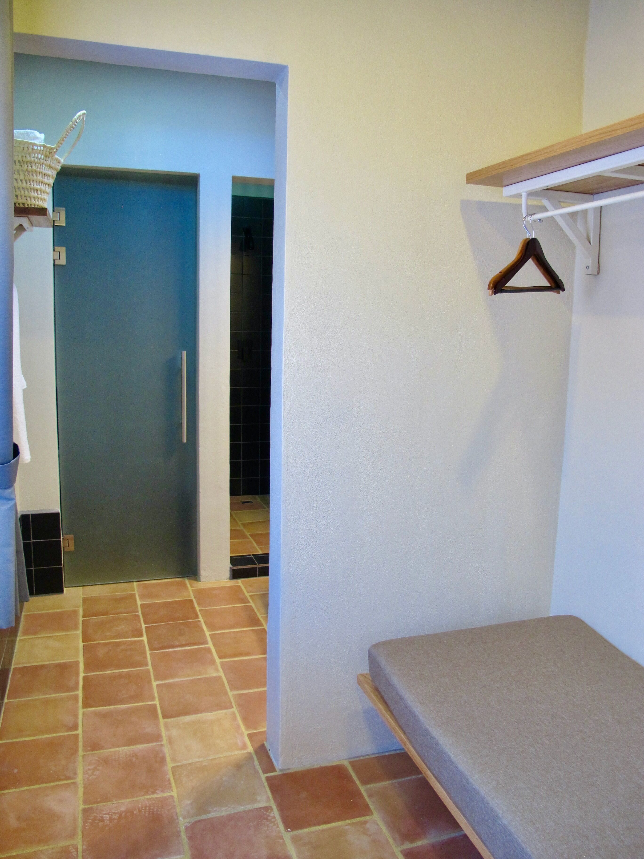 A compact room with a bench, a hanging clothes rack, and a door leading to another room.