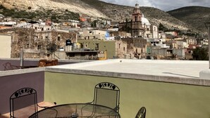A terrace with a table and chairs, overlooking a town with historic buildings and a prominent church.