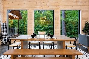 Une table à manger en bois, avec des chaises, un banc et une grande fenêtre donnant sur un paysage verdoyant.