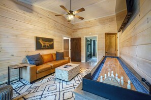A cozy room with a wooden ceiling, a brown leather sofa, a patterned rug, and a foosball table.