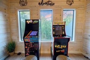 Two arcade machines in a room with wooden walls and large windows.
