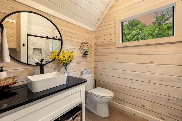 A wooden-paneled bathroom with a white sink, black countertop, and a round mirror.