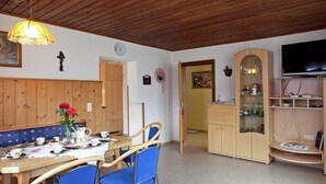 En matplats med ett träbord och stolar, en klocka på väggen och en tv i bakgrunden.