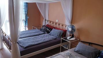 Ein Bett mit Baldachin, ein Nachttisch mit Ventilator und ein Fenster mit Vorhängen.
