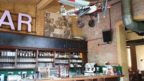 Eine Bar mit einer Kreidetafel, Regalen voller Flaschen und Gläsern, und einem hängenden Modellflugzeug.
