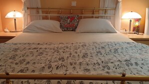 Ein Bett mit einem blumigen Überwurf, zwei Kissen, ein Zierkissen mit der Aufschrift 'LOVE' und einem Herz, sowie Nachttische mit Lampen auf beiden Seiten.