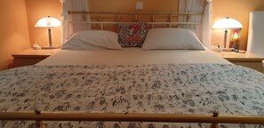 Ein Bett mit einem blumigen Überwurf, zwei Kissen, ein Zierkissen mit der Aufschrift 'LOVE' und einem Herz, sowie Nachttische mit Lampen auf beiden Seiten.