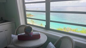 A small dining area with wicker chairs and a table, a window with a view of turquoise waters and islands, and a kitchen area with a sink and cabinets. - Hotel Sophia Boutique Hotel (St. Thomas)