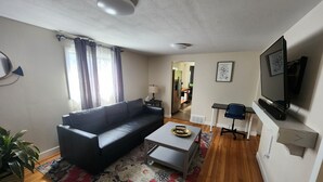 A living room with a black sofa, a coffee table, a TV, and a patterned rug.