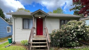 A single-story house with a red front door, a small front porch, and a front yard with a pathway leading to the door.