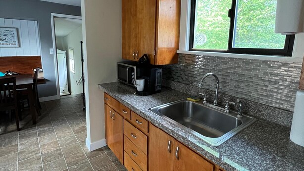 A kitchen with granite countertops, wooden cabinets, a stainless steel sink, and a window with a view of greenery.