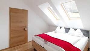 A bedroom with a wooden door, a bed with white bedding and a red blanket, and skylights. - Apartment in Hohentauern With Sauna (Hohentauern)
