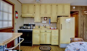 A compact kitchen with a stove, sink, and refrigerator, wooden cabinets, and a small dining area.