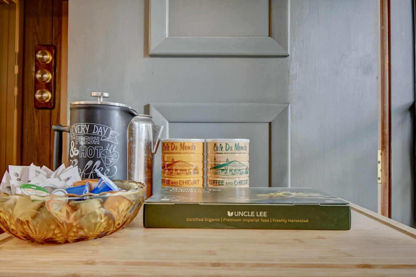 A kitchen counter with a coffee maker, canned coffee, a bowl of snacks, and a box of tea.