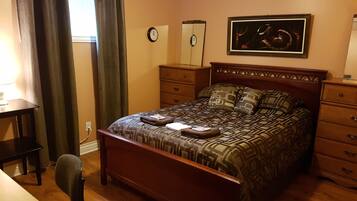 A bedroom with a wooden bed, a desk, a chair, a dresser, and a painting on the wall.