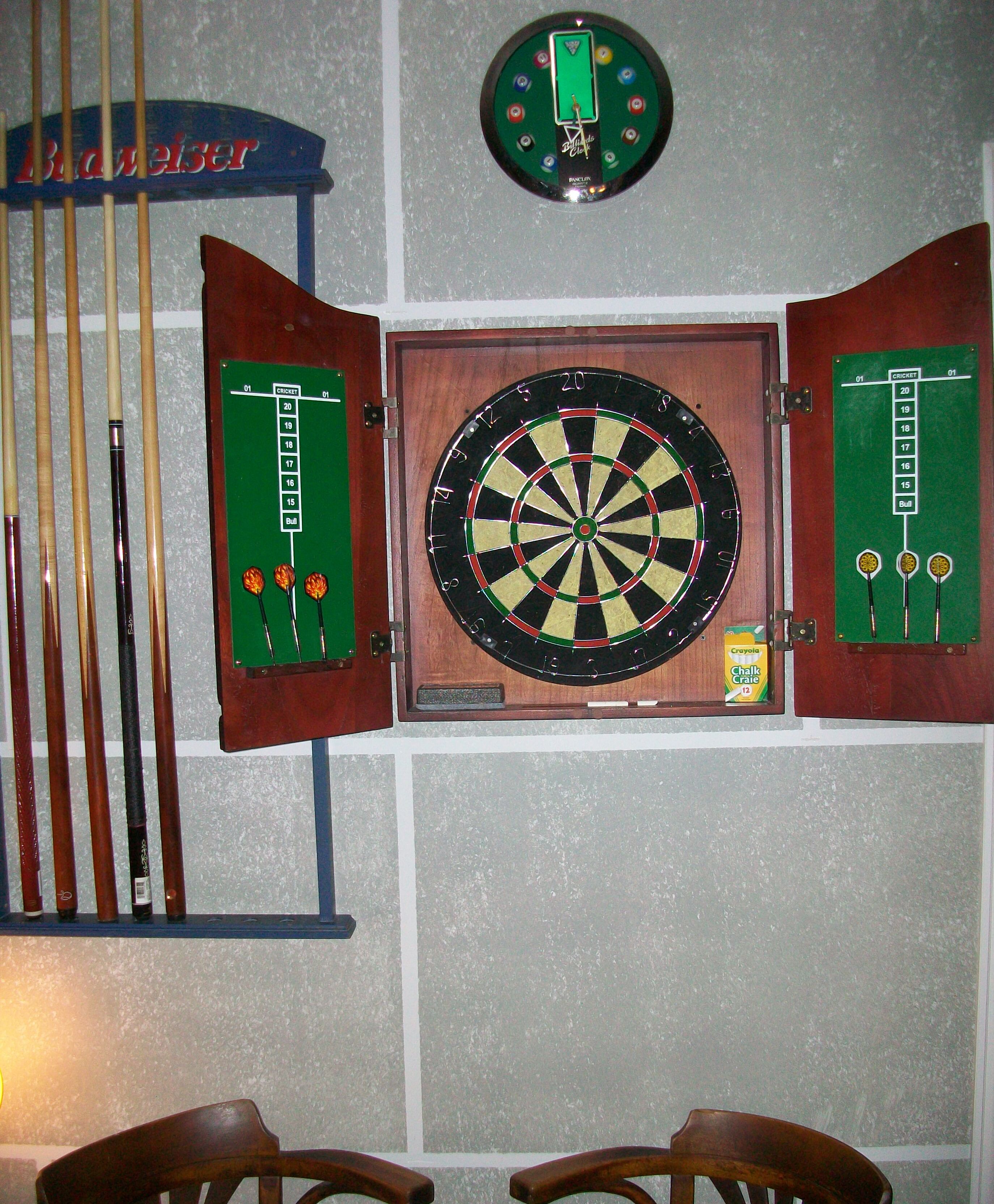 A dartboard mounted on a wall with a dartboard case and darts beside it.