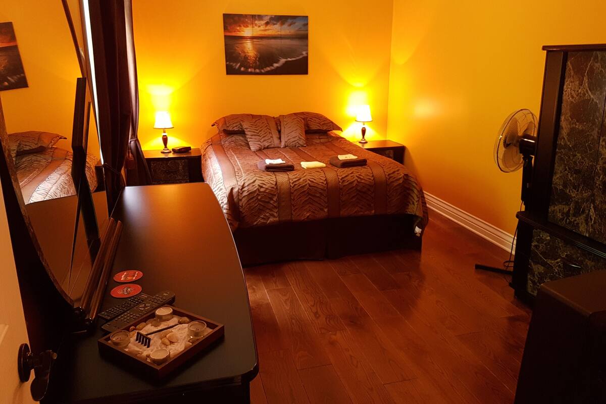 A hotel room with a bed, bedside lamps, a painting on the wall, and a wooden floor.