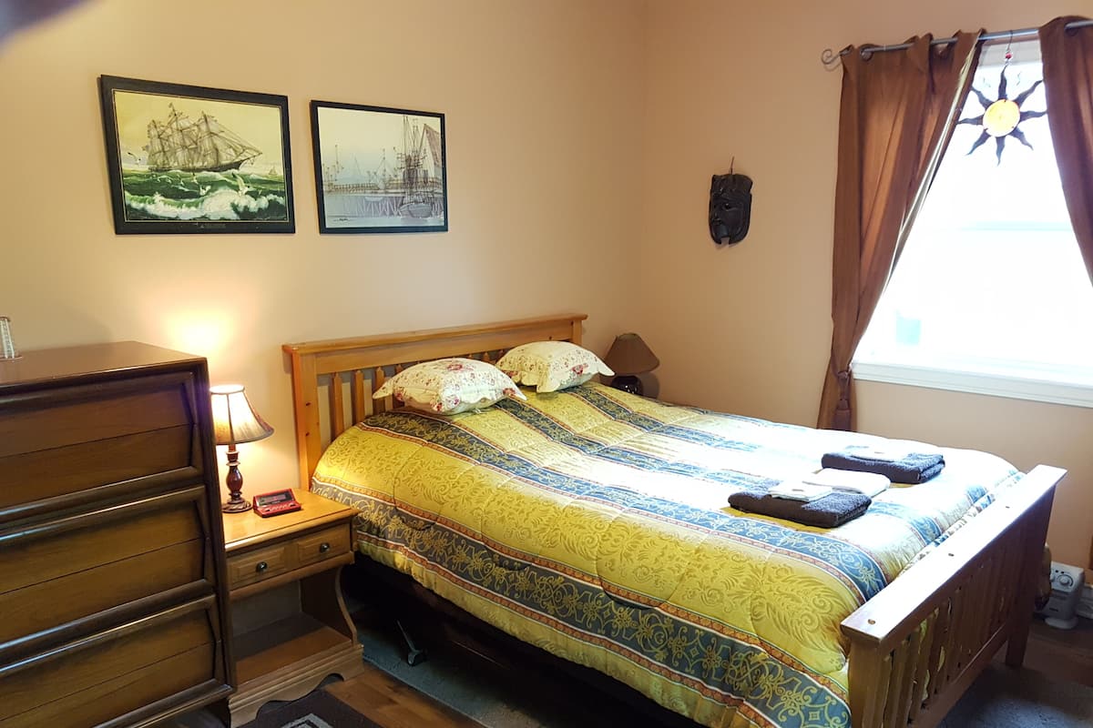 A bedroom with a wooden bed, a nightstand with a lamp, a dresser, and two framed pictures on the wall.