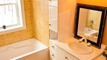 A bathroom with a white bathtub, a sink with a mirror, and a window.
