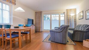 Una sala de estar moderna con una mesa de comedor de madera, sillas azules, un sofá gris y una televisión.