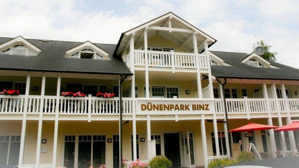 Un hotel con balcón, un cartel que dice "DÜNENpark Binz" y un cielo despejado.