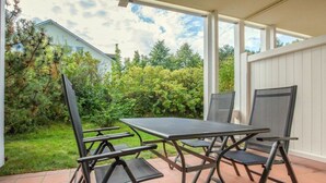 Un patio exterior con una mesa y sillas, rodeado de un jardín y una valla blanca.