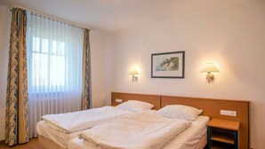 Una cama doble con dos mesitas de noche, una ventana con cortinas, y un cuadro en la pared.