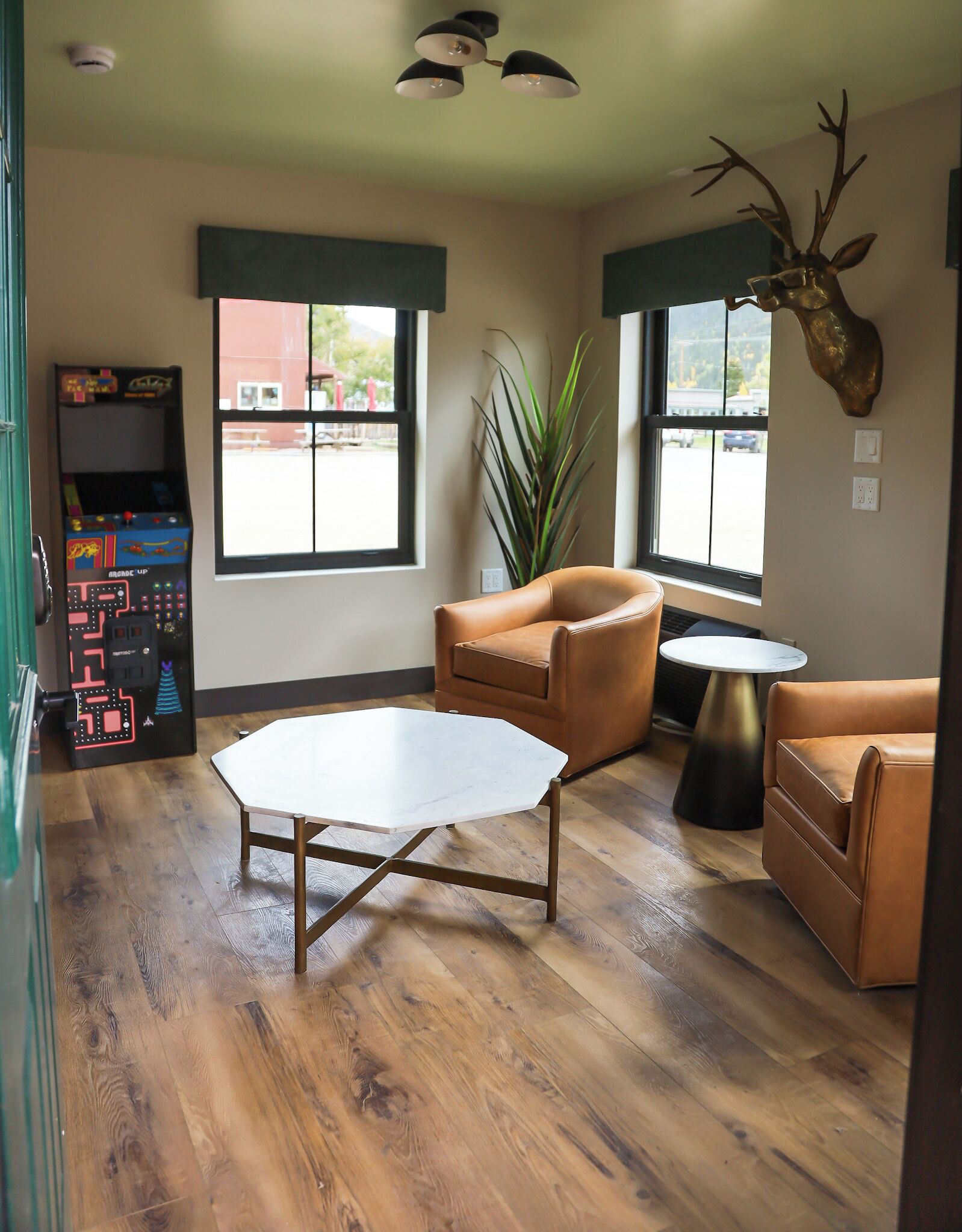 A room with a wooden floor, a white octagonal table, two brown leather sofas, a small round table, and a large window with a view of a building outside.