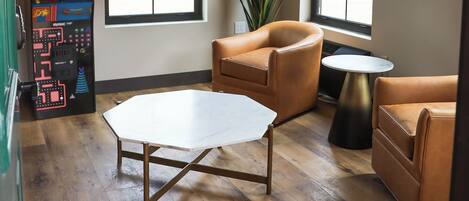A room with a wooden floor, a white octagonal table, two brown leather sofas, a small round table, and a large window with a view of a building outside.