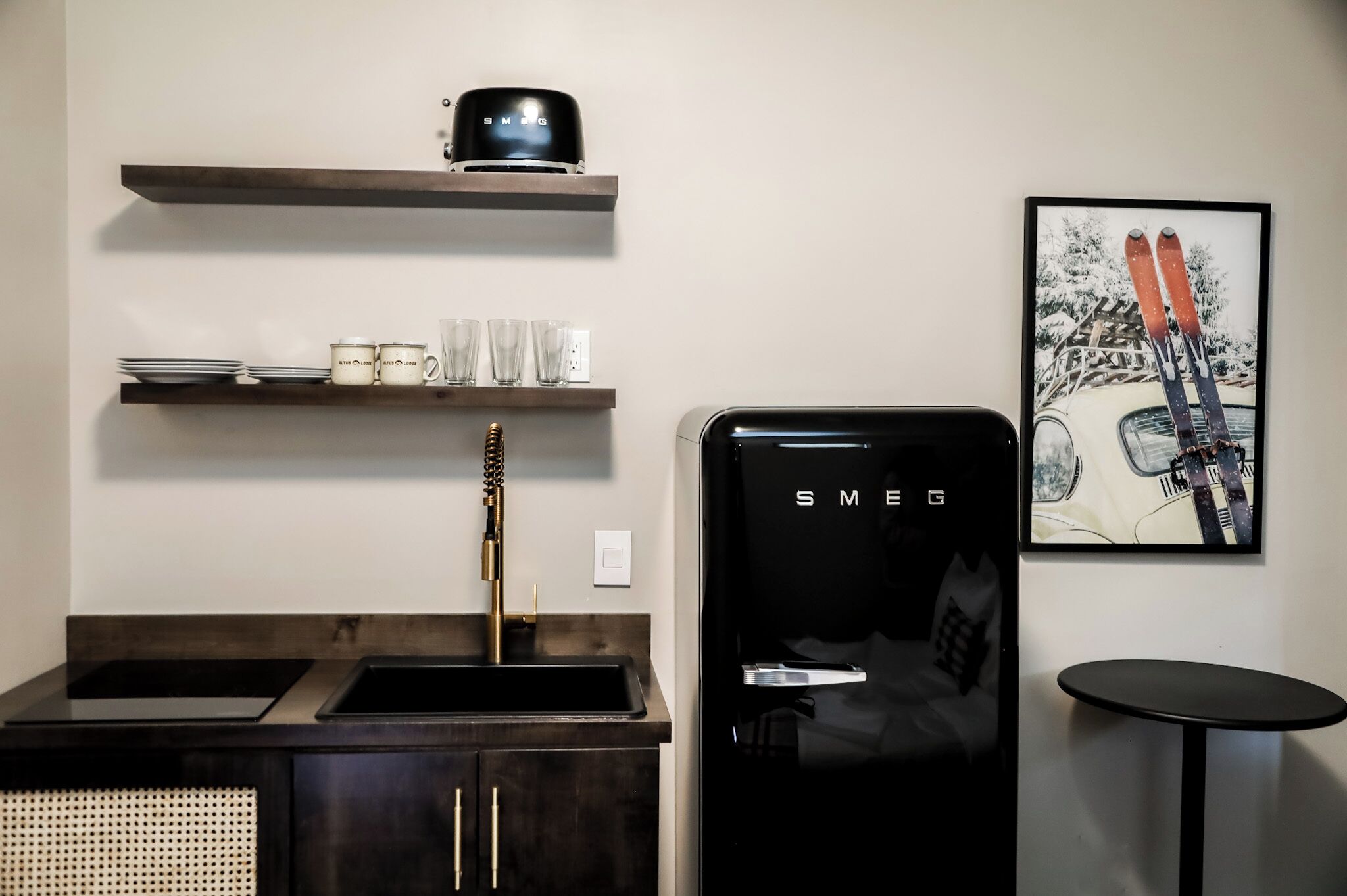 Una cocina con un refrigerador negro, una cafetera en un estante y un cuadro con esquíes en la pared.