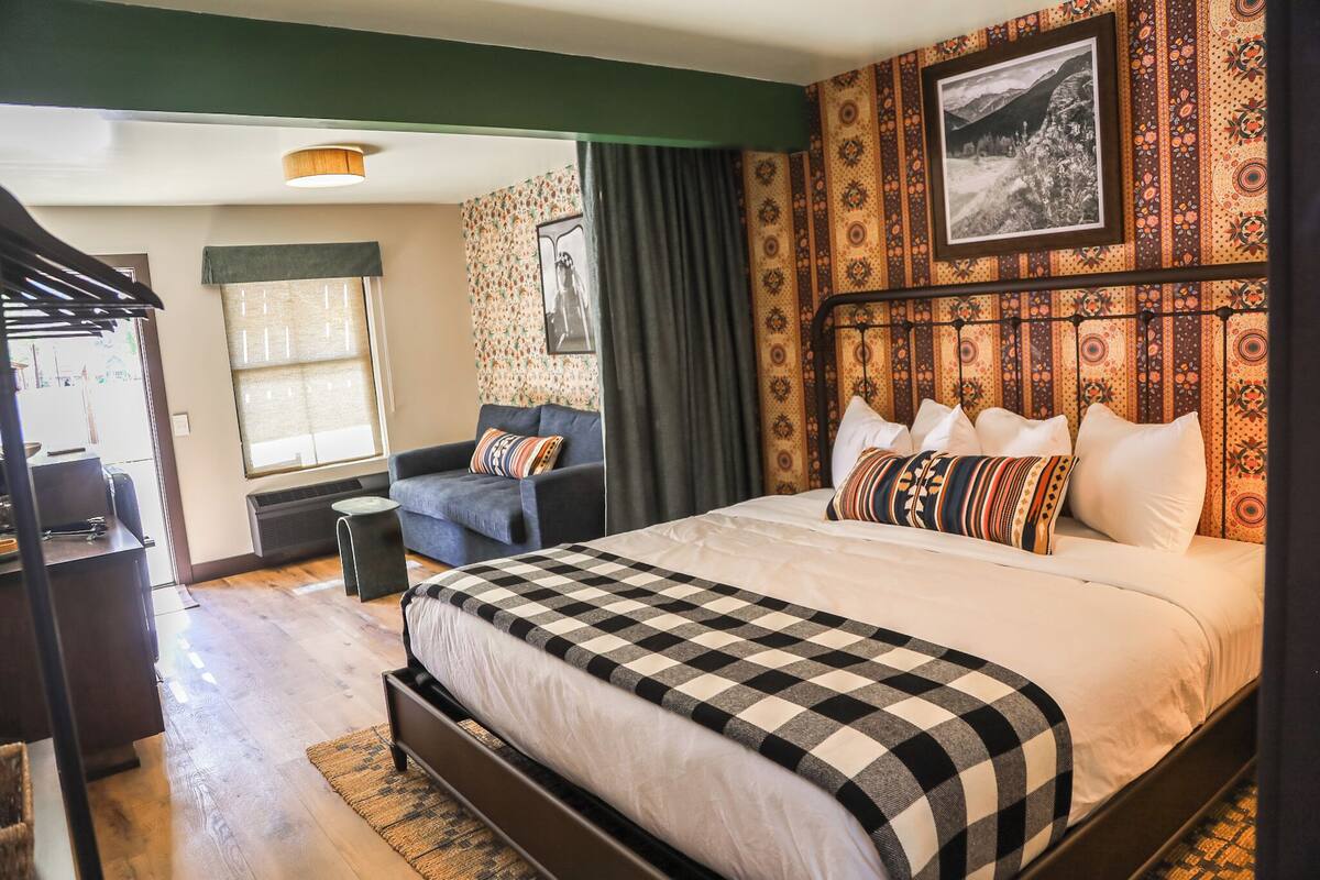 A bedroom with a large bed, a sofa, a small table, and a window with curtains.