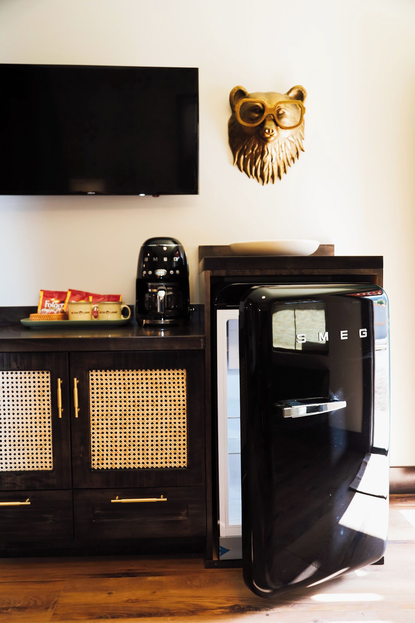 Une cuisine avec un réfrigérateur noir, une machine à café et un téléviseur fixé au mur.