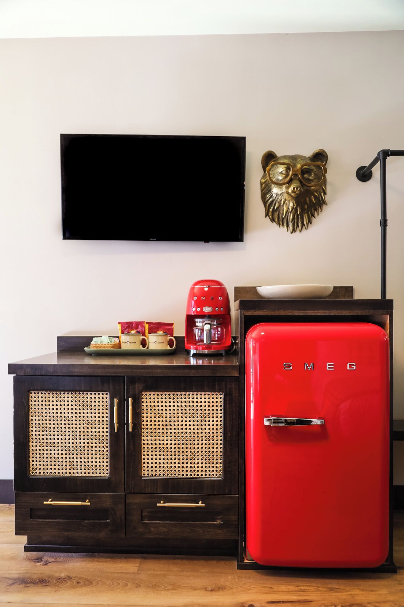 Una sala de estar moderna con un mueble de madera oscura, un refrigerador rojo de estilo vintage, una cafetera y un televisor montado en la pared.